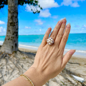 Hand wearing a white akoya pearl cluster ring with a Hawaiian beach and palm tree in the background