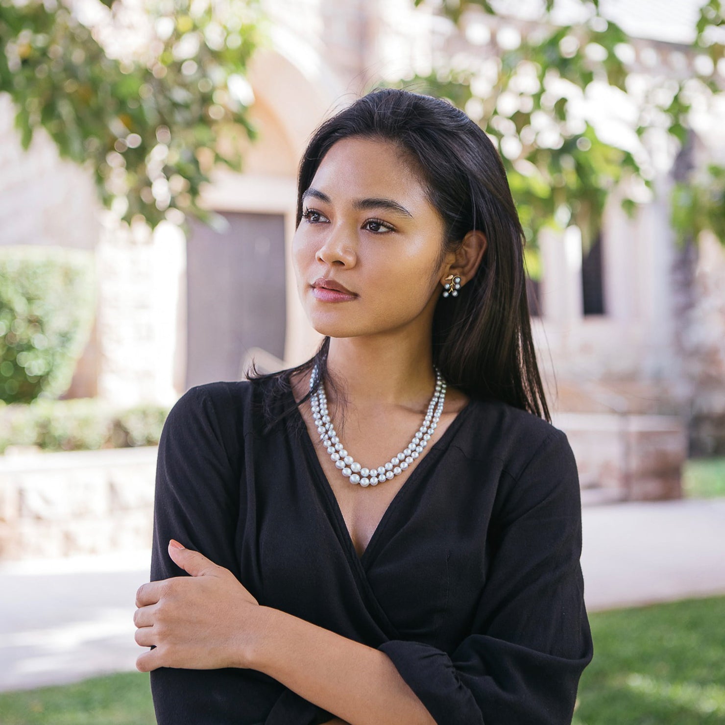 Japanese model wearing a dress and a double strand akoya pearl necklace and earrings in a courtyard with a blurred background.