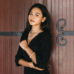 Beautiful Japanese model wearing a black outfit with a white saltwater akoya pearl necklace and bracelet against a wooden background.